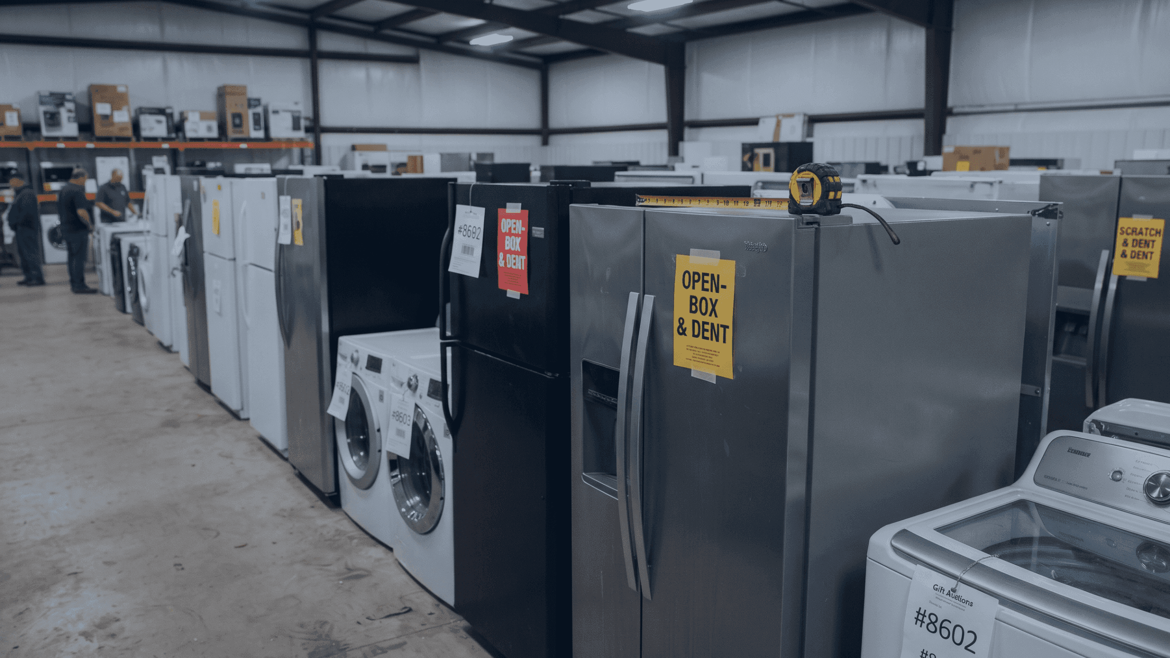 Rows of refrigerators and washing machines displayed in a warehouse appliance store.
